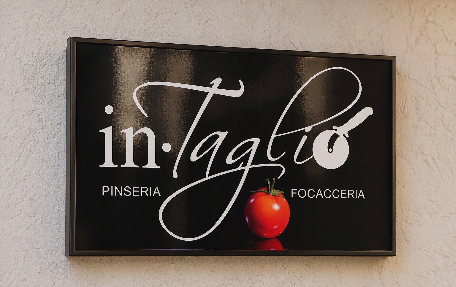 L'insegna in·Taglio pinseria focacceria sul muro chiaro