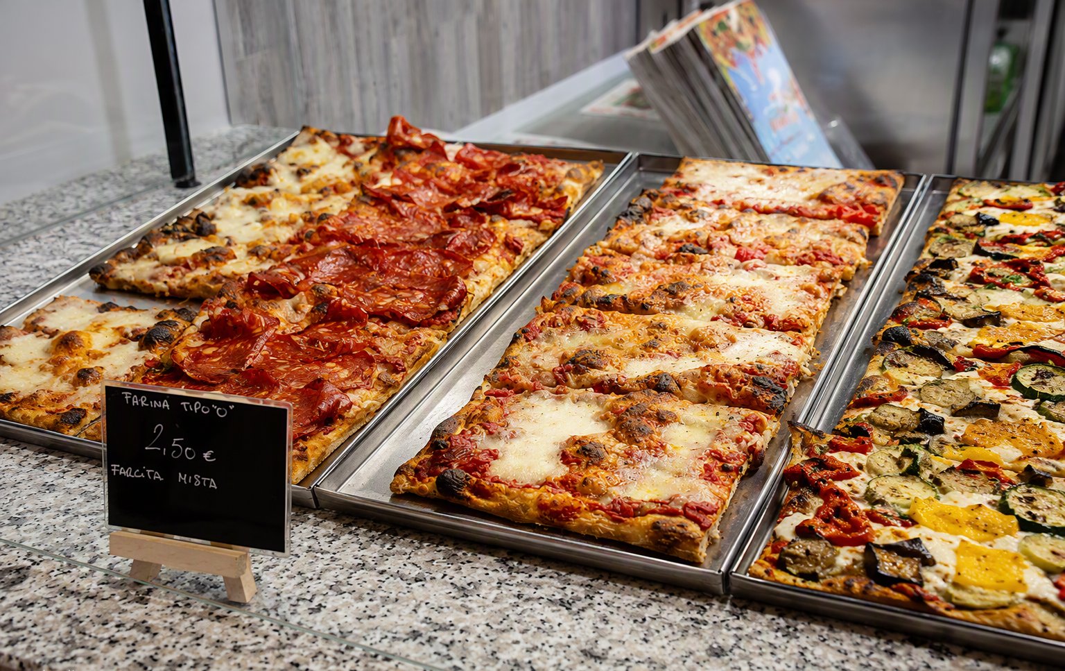 Il banco con le teglie di pizza al taglio e la lavagnetta con il prezzo